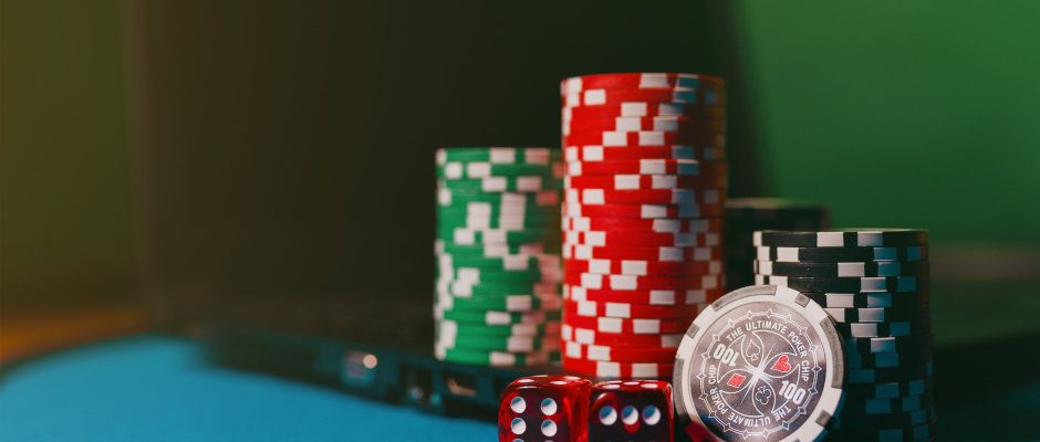 Fichas de cassino e dados sobre uma mesa, ao lado de um laptop, em referência às apostas online.