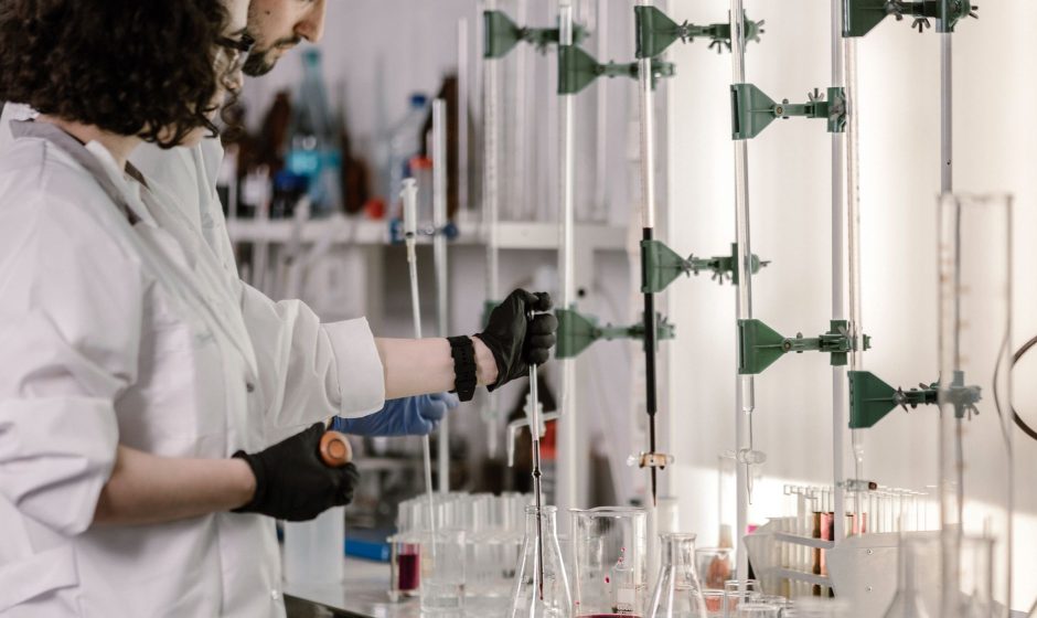 Dois pesquisadores de jaleco trabalham com tubos de ensaio em um laboratório moderno.