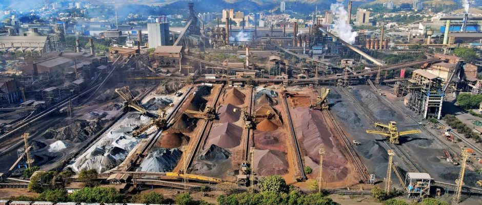 Vista ampla de uma instalação industrial de mineração, com máquinas e pilhas de rejeitos.