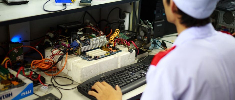 Técnico trabalha em uma placa-mãe sobre uma bancada de laboratório.