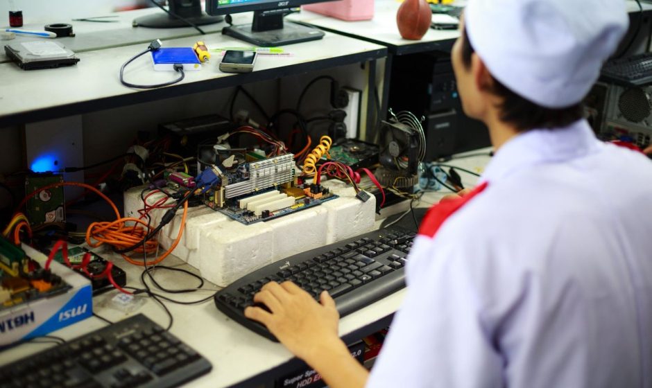 Técnico trabalha em uma placa-mãe sobre uma bancada de laboratório.
