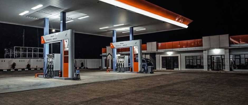 Posto de combustíveis contemporâneo iluminado à noite, com bombas sob a cobertura.