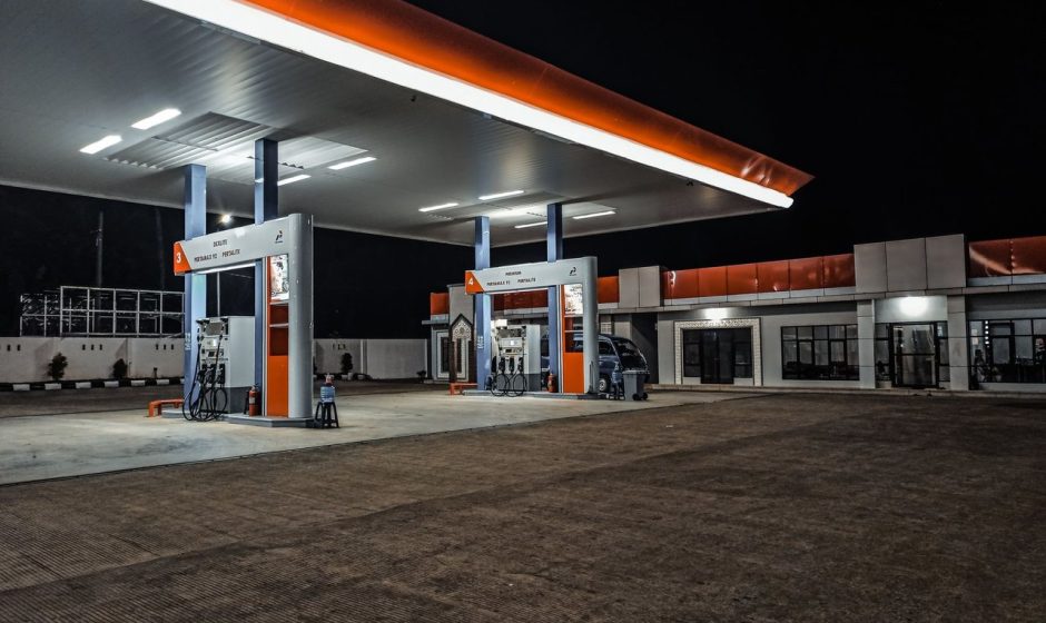 Posto de combustíveis contemporâneo iluminado à noite, com bombas sob a cobertura.
