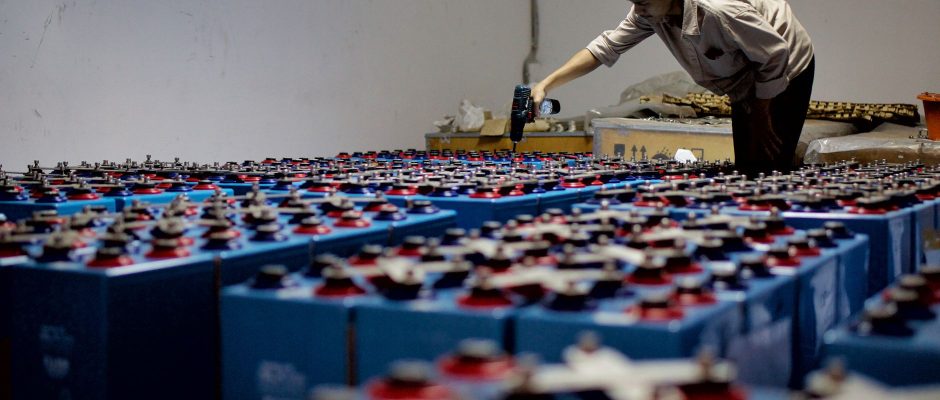 Trabalhador inspeciona baterias industriais em uma instalação fabril.