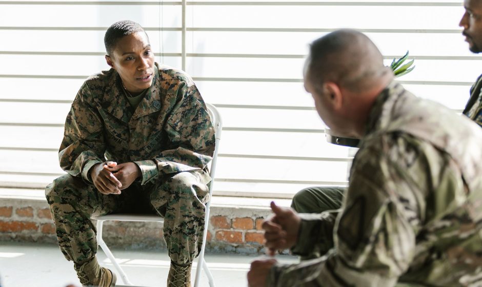 Profissionais da área militar participam de uma sessão de terapia em grupo em ambiente interno.